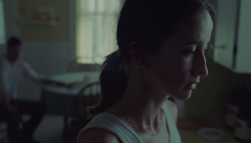 Woman in profile indoors with a blurred man in the background