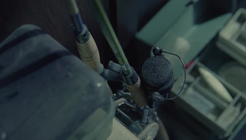 A close view of professional fishing rods and a black reel with thin line inside a storage area with other tackle gear