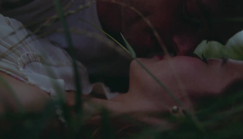 Couple kissing while lying on grass among leaves and vegetation