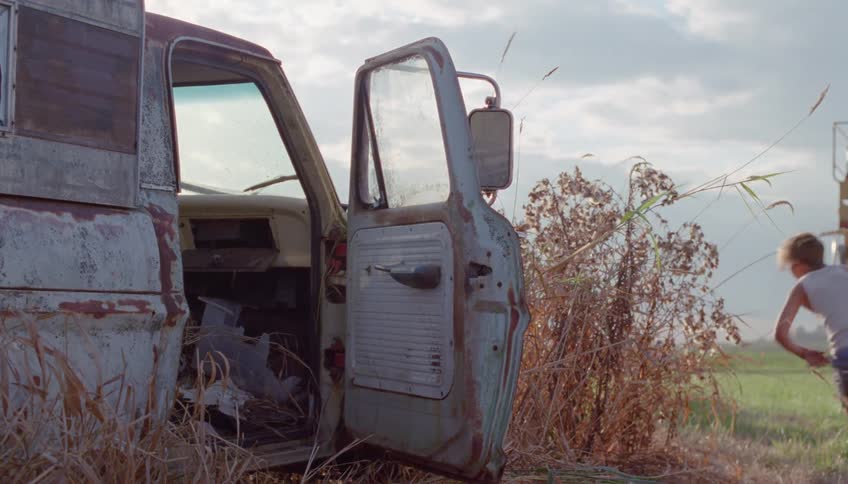 A boy standing next to an old rusted truck gets scared and runs off