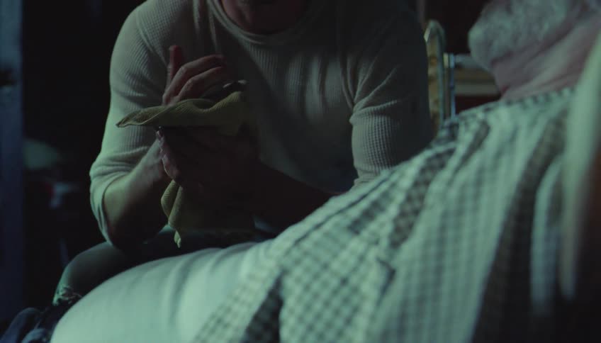 An elderly man in a bed with a man sitting next to him in the hospital