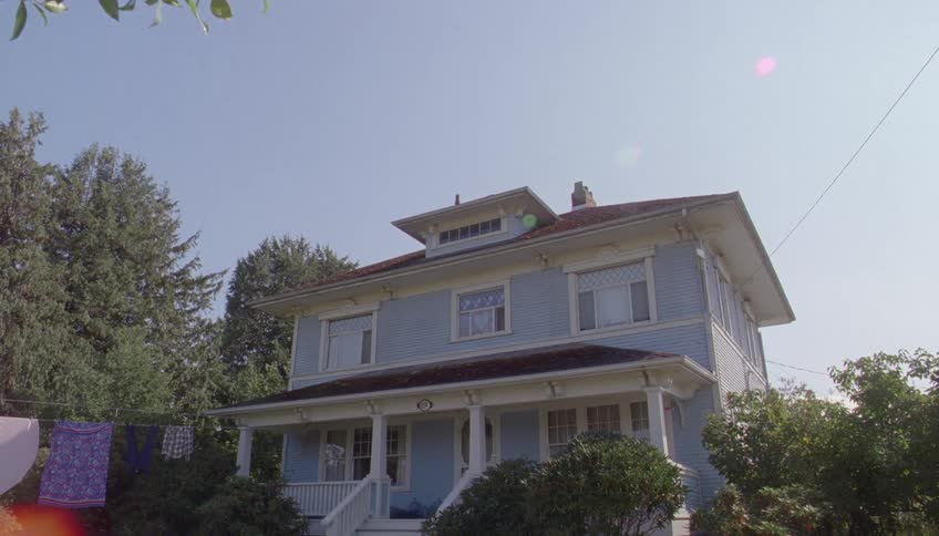 A large two story suburban house with a front porch surrounded by trees and bushes