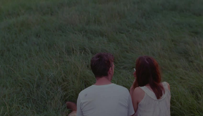 Woman smokes while sitting and laughing in a field with a male friend on a summer day