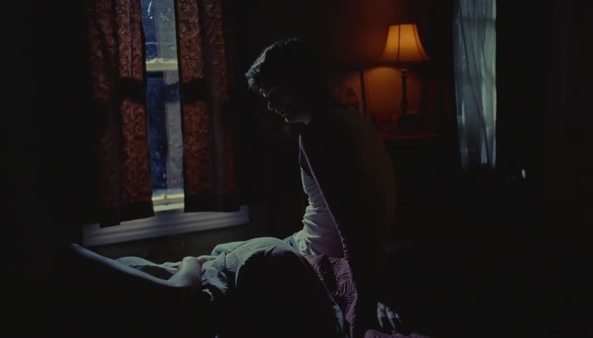 An upset couple sitting in silence on a bed in a dimly lit bedroom at night