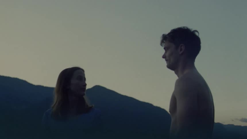 Couple embraces in the sea with mountains in the background at dusk