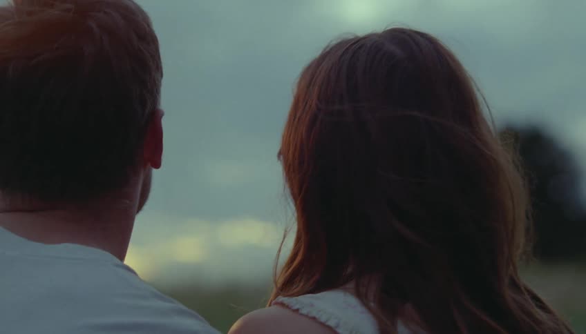 A romantic couple stands close together deeply gazing into each others eyes at dusk