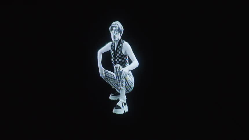 A person wearing checkered clothing and platform shoes crouches and poses against a dark background the footage features a distorted glowing aesthetic that resembles a lofi digital hologram or a thermal image