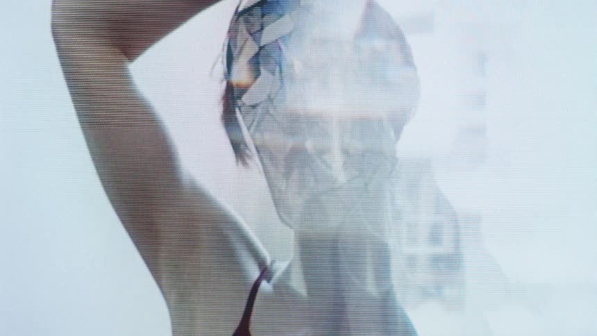 Woman wearing a translucent geometric mask raises her arm under intense lighting