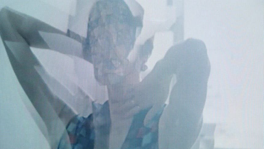 Woman wears a translucent facial mask with arms raised in a brightly lit environment