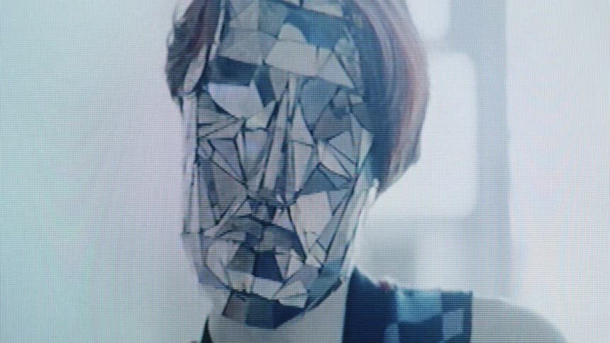 A person wearing a mask of small geometric mirror shards performing slow eerie hand movements