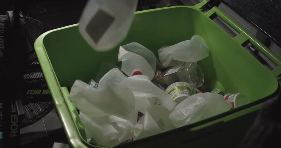 Plastic water jugs are collected in a green recycling bin in an industrial environment