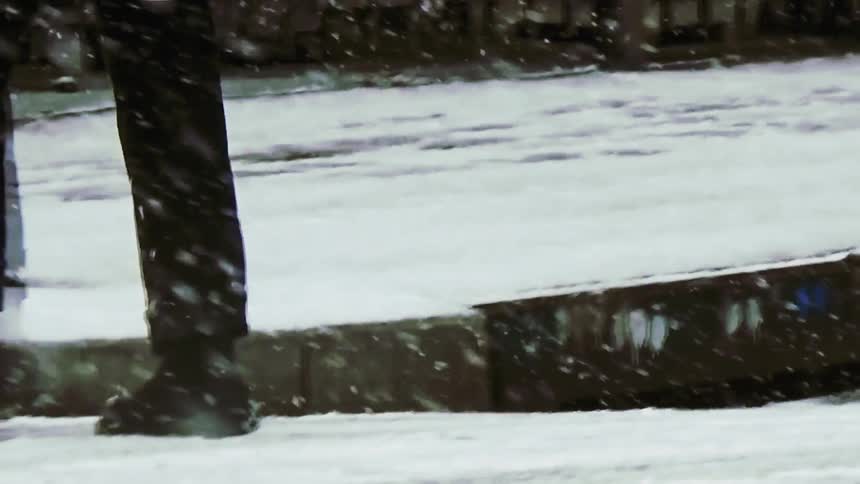 Car drives past after a pedestrian crosses a snowy street during a winter snowfall