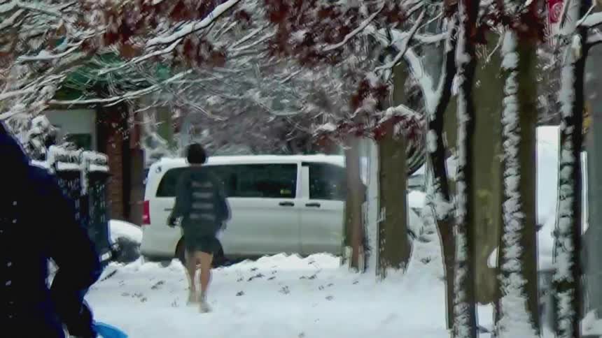 A runner jogs down a snow covered tree lined sidewalk