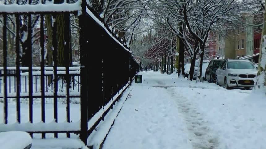 Snowcovered sidewalk beside a fenced park and residential street