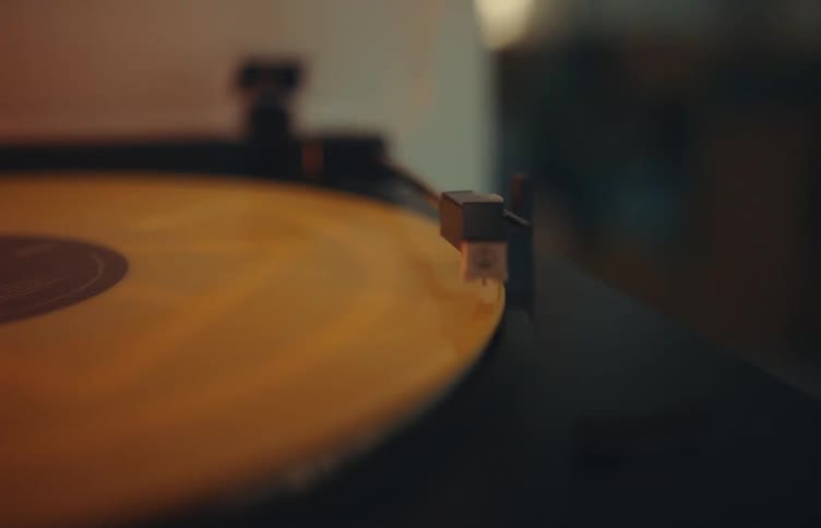 Closeup of record player needle resting on a spinning vinyl record in a softly lit room