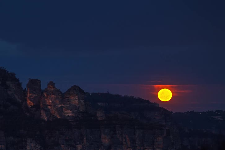 Full moon rising over mountains behind clouds