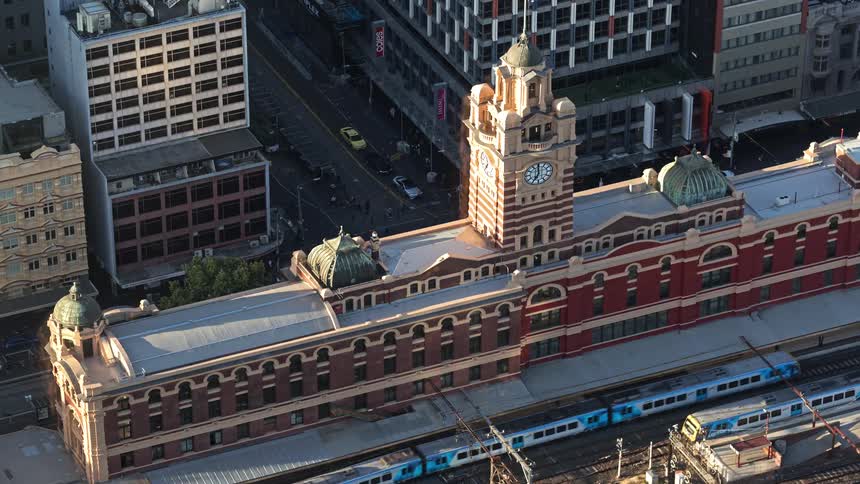 Trains pass by a building with a clock tower as traffic moves on the city streets