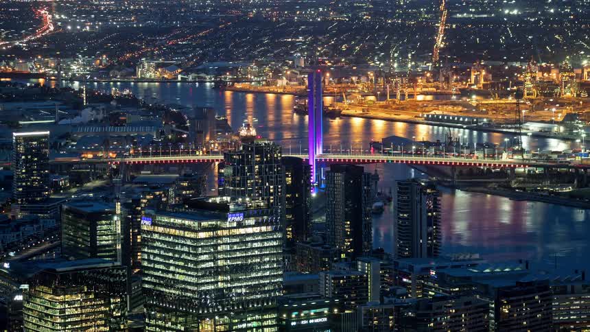 Lit bridge over river with skyscrapers and industrial zone
