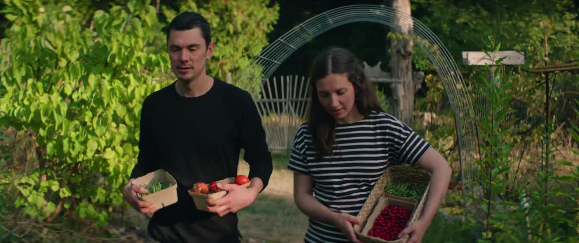 Man and woman walking through a garden carrying baskets of produce