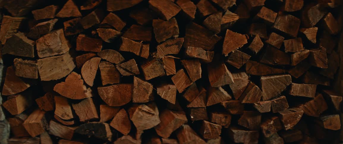 The video shows a closeup static shot of a large stack of chopped firewood since the image is a dense pile of irregular wood pieces