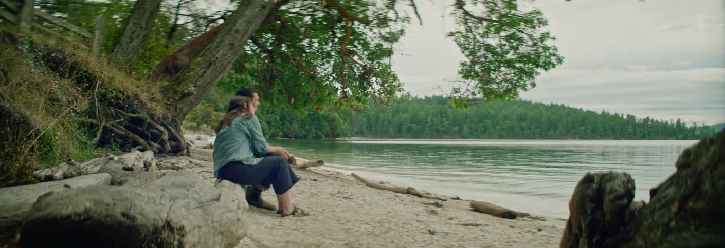 Young adult couple sitting on a trunk next to a river with a forest on the background outdoors during day time