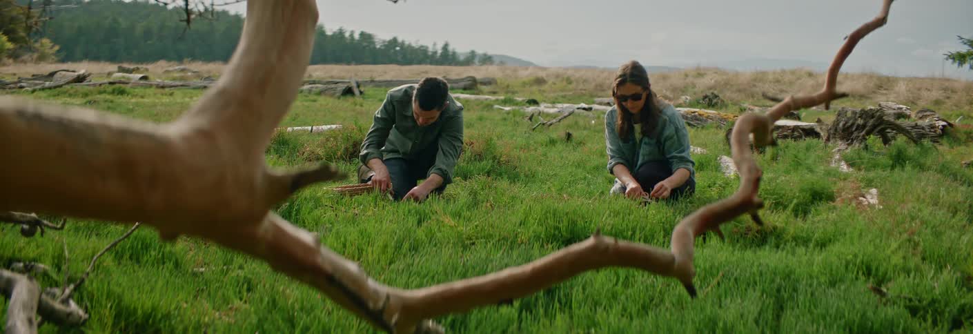 Two people kneeling on green field surrounded by branches and forest