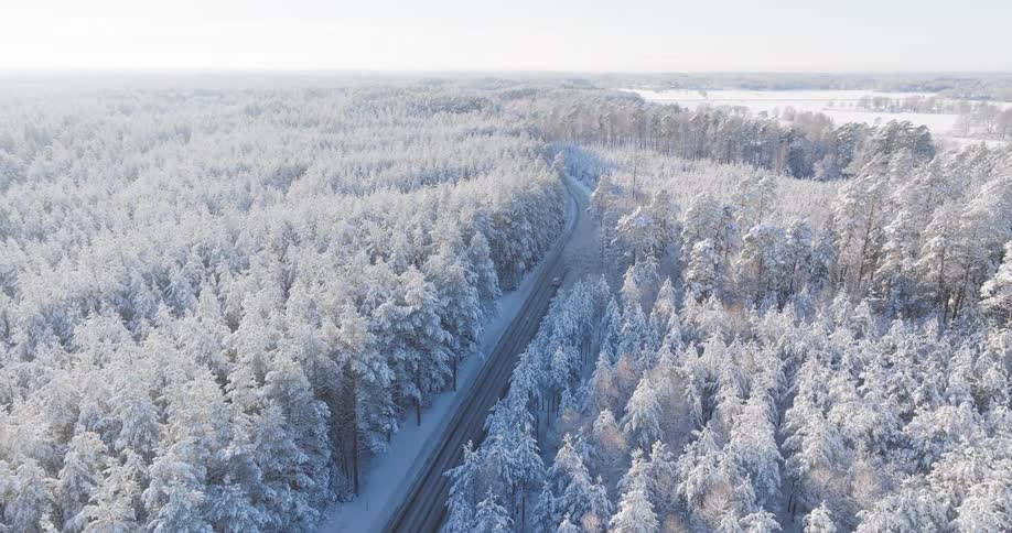 Aerial view of a vehicle traveling along a highway surrounded by a snowcovered forest
