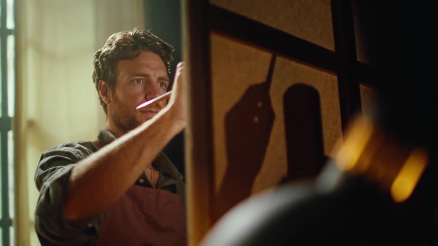 The man is painting on the canvass