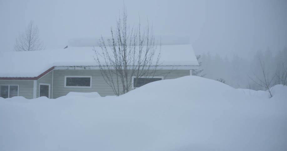 A neighborhood is buried under massive snowdrifts during a heavy winter storm the camera pans across houses vehicles and heavy machinery almost completely submerged in deep snow