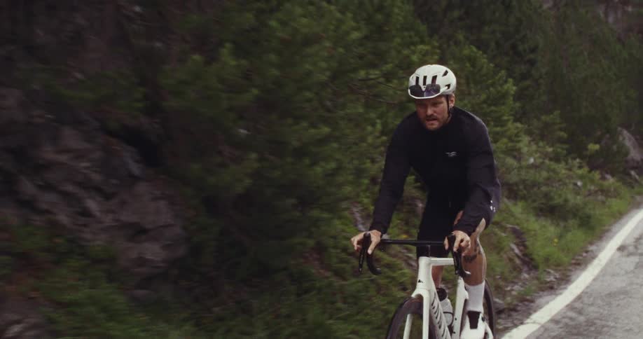 Cyclist wearing a white helmet rides on a paved road surrounded by green vegetation