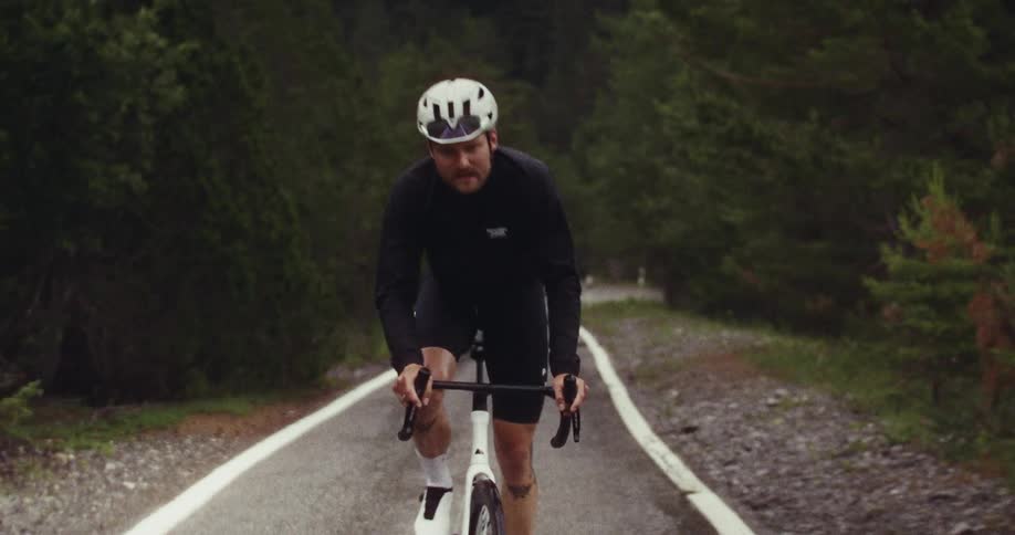 Cyclist rides on a winding rural road surrounded by dense vegetation