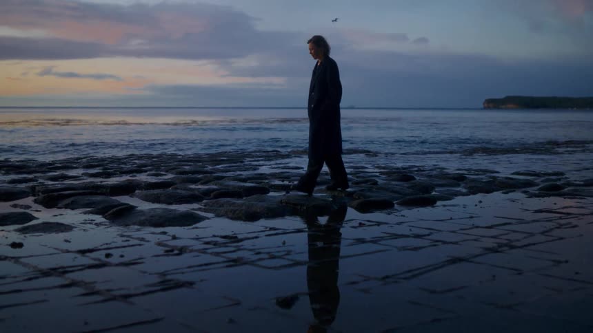 A young woman walking on the beach wearing nightwear at sunset