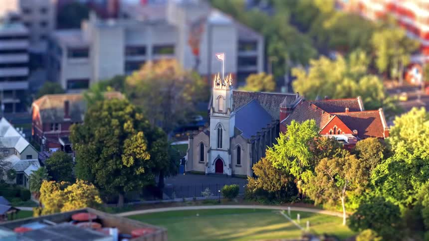 Church with a central tower and a flag on top surrounded by trees and residential buildings