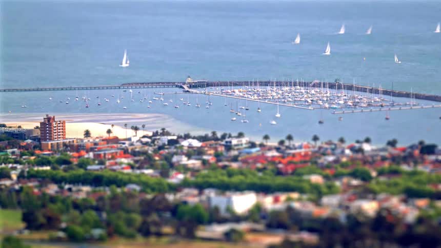 Coastal marina with docked boats and sailboats offshore with an urban area in the foreground