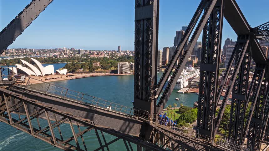 A group of climbers in blue suits ascends the sydney harbour bridge high above the harbour and the sydney opera house