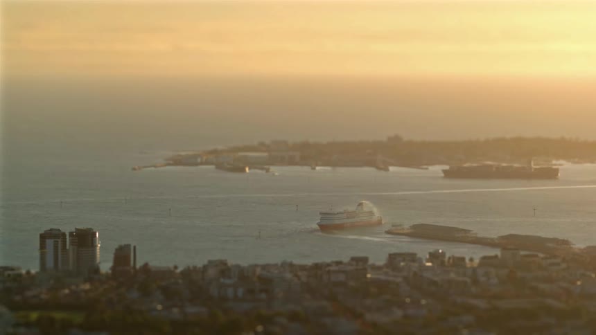 Aerial view of a ferry moving across a coastal bay near a metropolitan shoreline at sunset