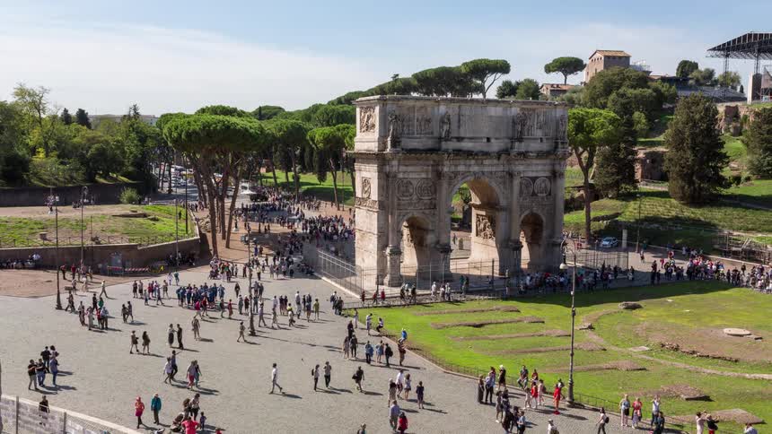 Aerial view of crowd walking around the arch of constantine in a historic city square