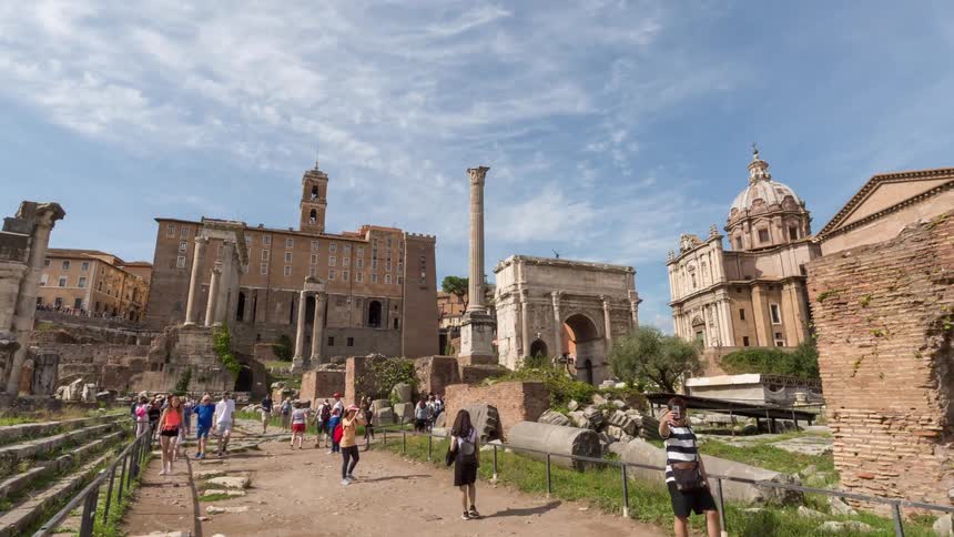 Tourists walk through the ancient ruins of a historic forum beneath a clear sky