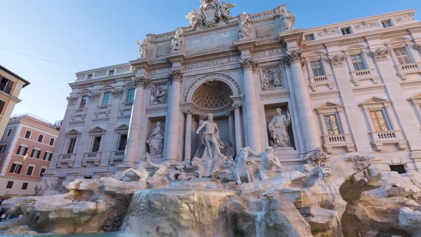 Tourists gathered near an ornate baroque fountain and historic building in a busy city square