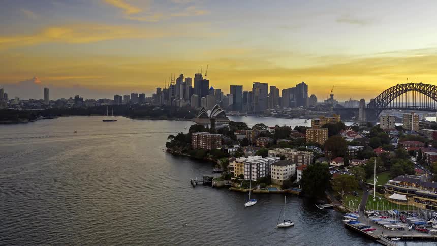 Aerial view of a metropolitan harbor skyline at dusk with a large bridge and waterfront buildings