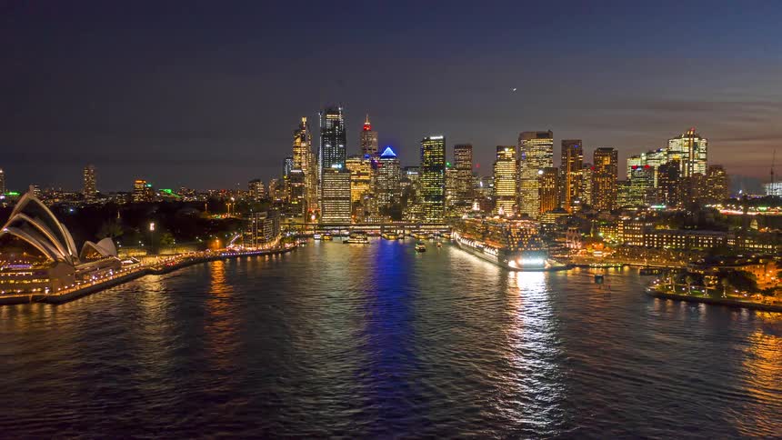 Illuminated skyscrapers and the sydney opera house glow as boats traverse the harbor at night