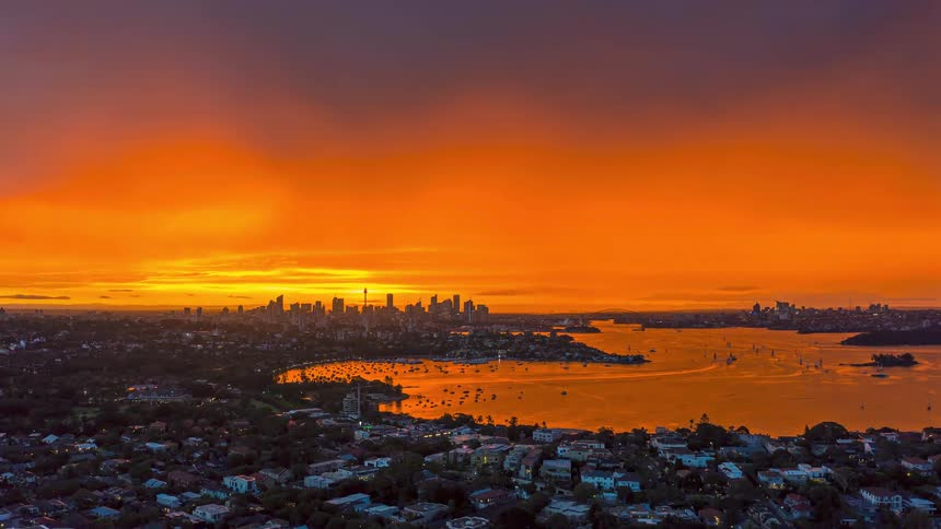 Aerial view of a coastal city as the sun sets below the horizon