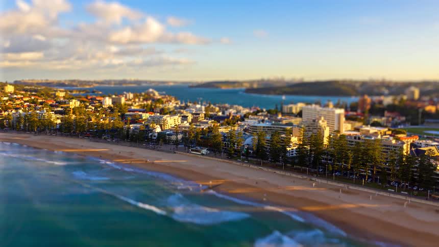 Aerial view of a coastal city with a sandy beach and rolling waves stretching along the shoreline in warm daylight