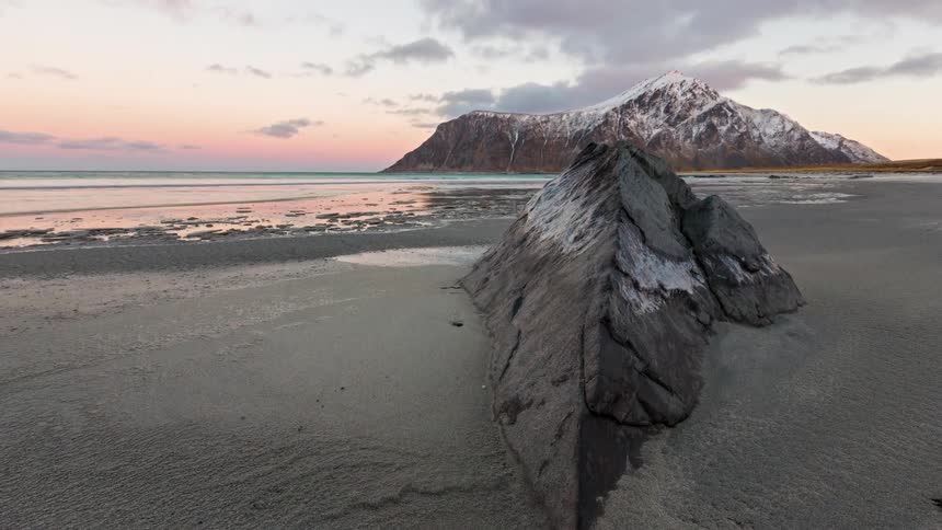 Aerial of a mountain and a giant rock formation on an ocean coast at sunset
