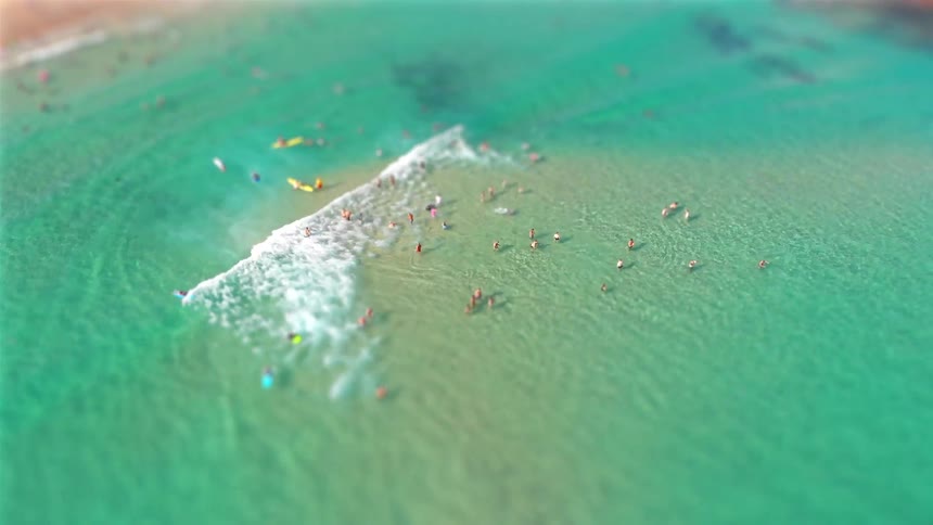 People swimming in clear water with inflatable rafts as waves roll in to shore
