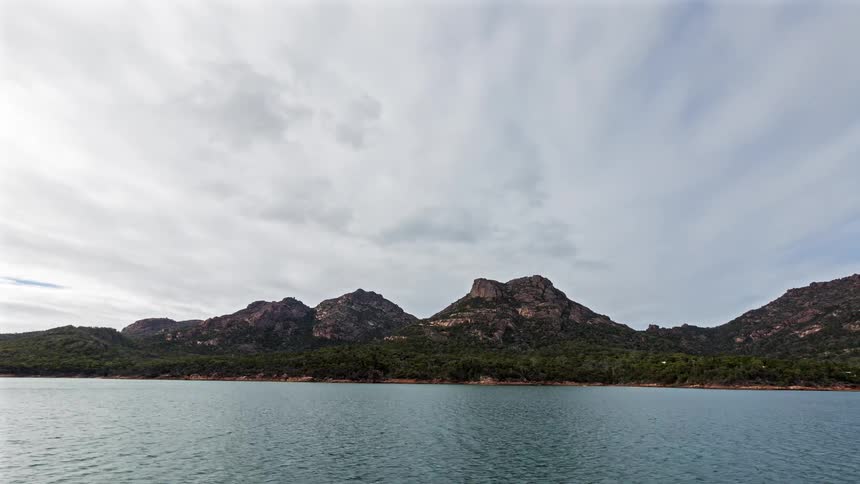 Calm water stretches toward a dark rugged island shoreline beneath a heavy overcast sky