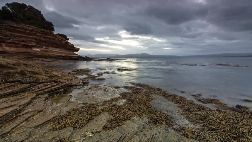 Small waves roll into a rocky beach near cliffs