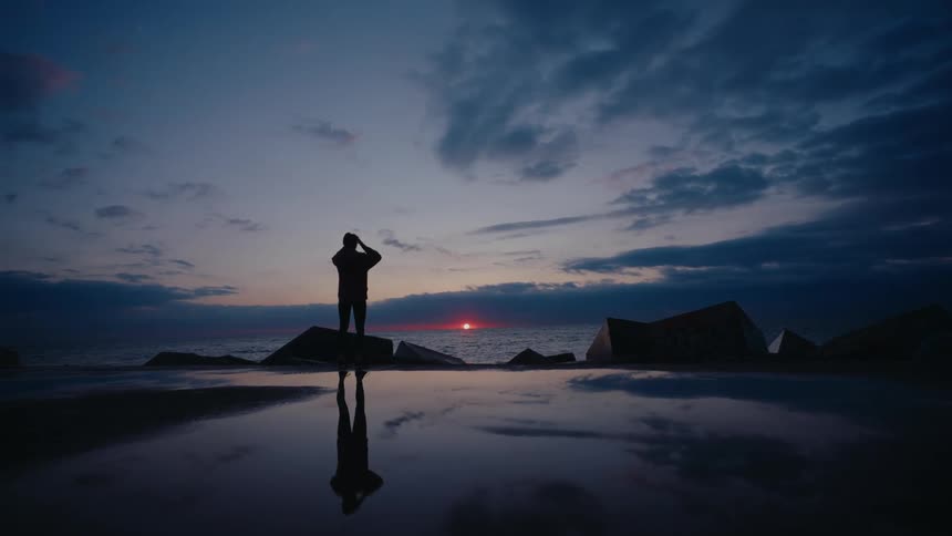 Woman silhouetted on breakwater blocks by the sea during sunset on the horizon