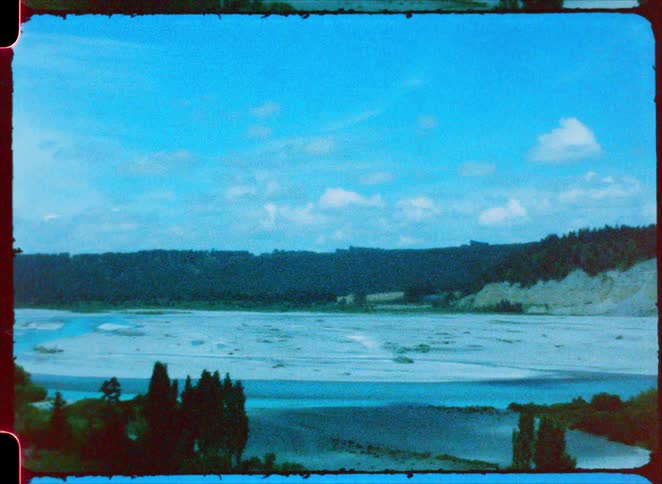 Floodplain with green areas and hills in the background under a blue sky