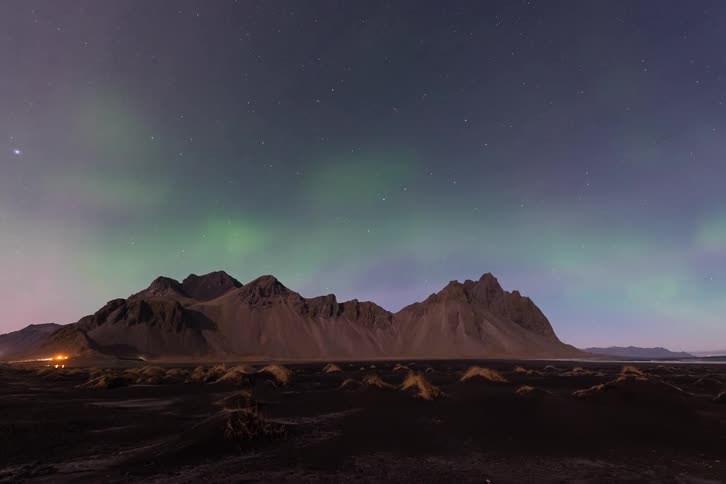 Green lights of the aurora borealis glow in a starry sky over mountains on the coast
